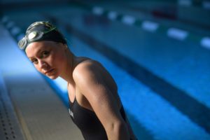 A portrait of a swimmer with blue light reflecting on a lane of the pool behind her.