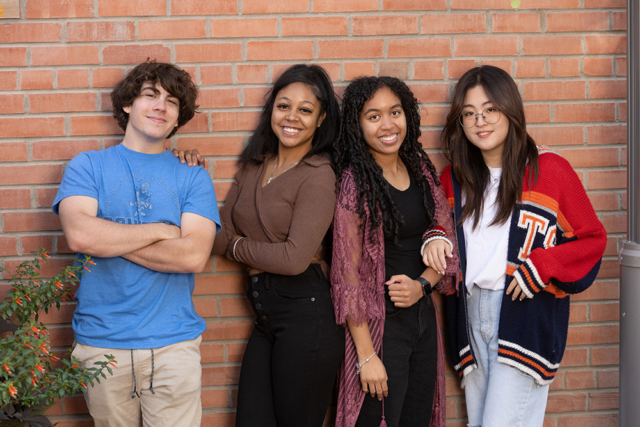 Student vloggers Frankie, Tiaira, Amanda and Jenny posing for a photo in front of a brick wall