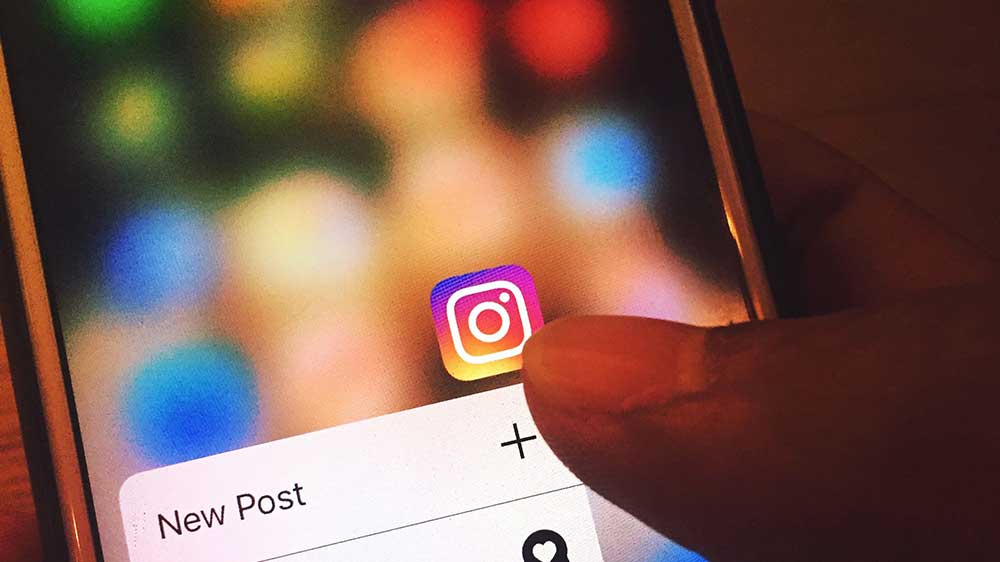 A thumb pressing on an Instagram app icon on an iPhone.