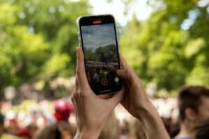 A close-up of hands holding up a phone that is recording a video of a crowd.