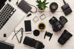 Set of modern photographic equipment on white wooden table, top view. Professional tools of creative designer, including memory cards and camera lenses. Equipment laying on white, wooden table. 